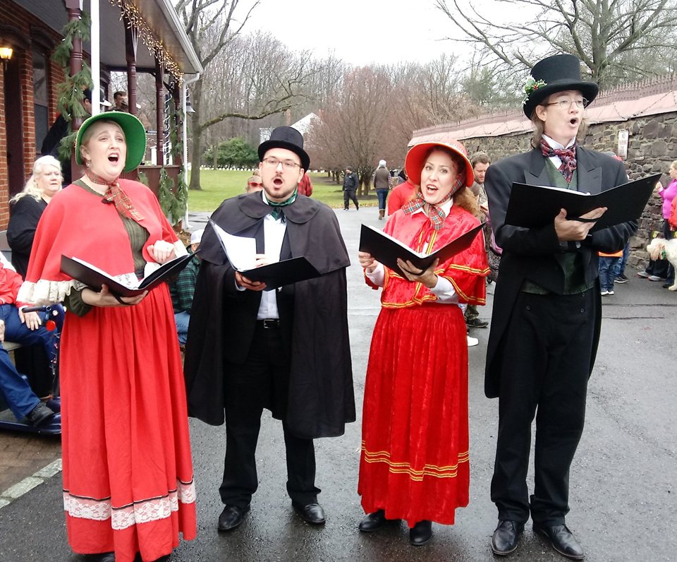 Quartet in red capes and top hats caroling outdoors