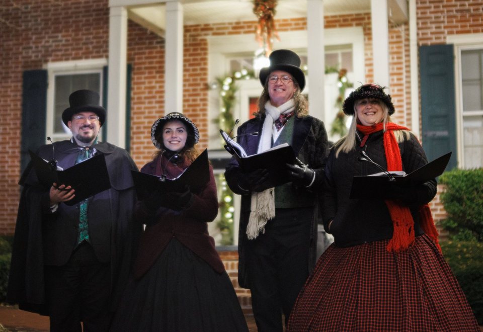 Carolers smiling in front of a decorated brick house