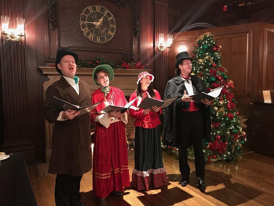 Carolers performing beside a Christmas tree in a paneled room